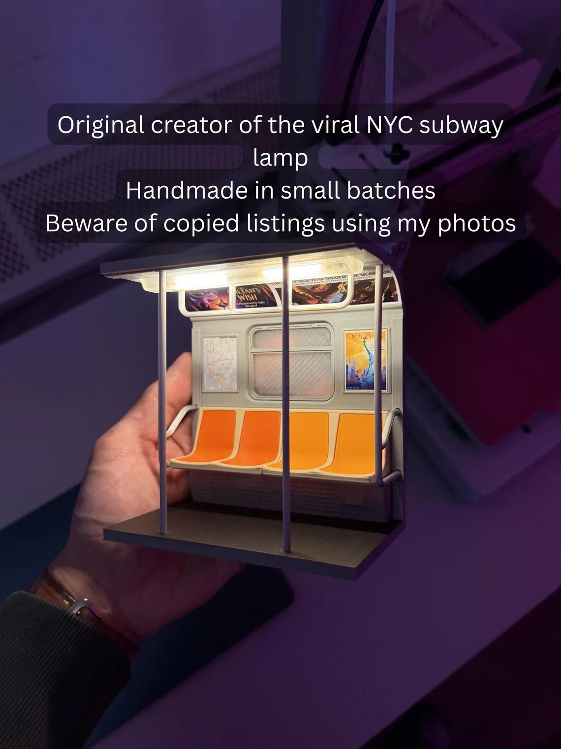 May include: A miniature NYC subway lamp with orange seats and posters. The lamp is handmade and features the text "Original creator of the viral NYC subway lamp". The lamp is held in a person's hand.