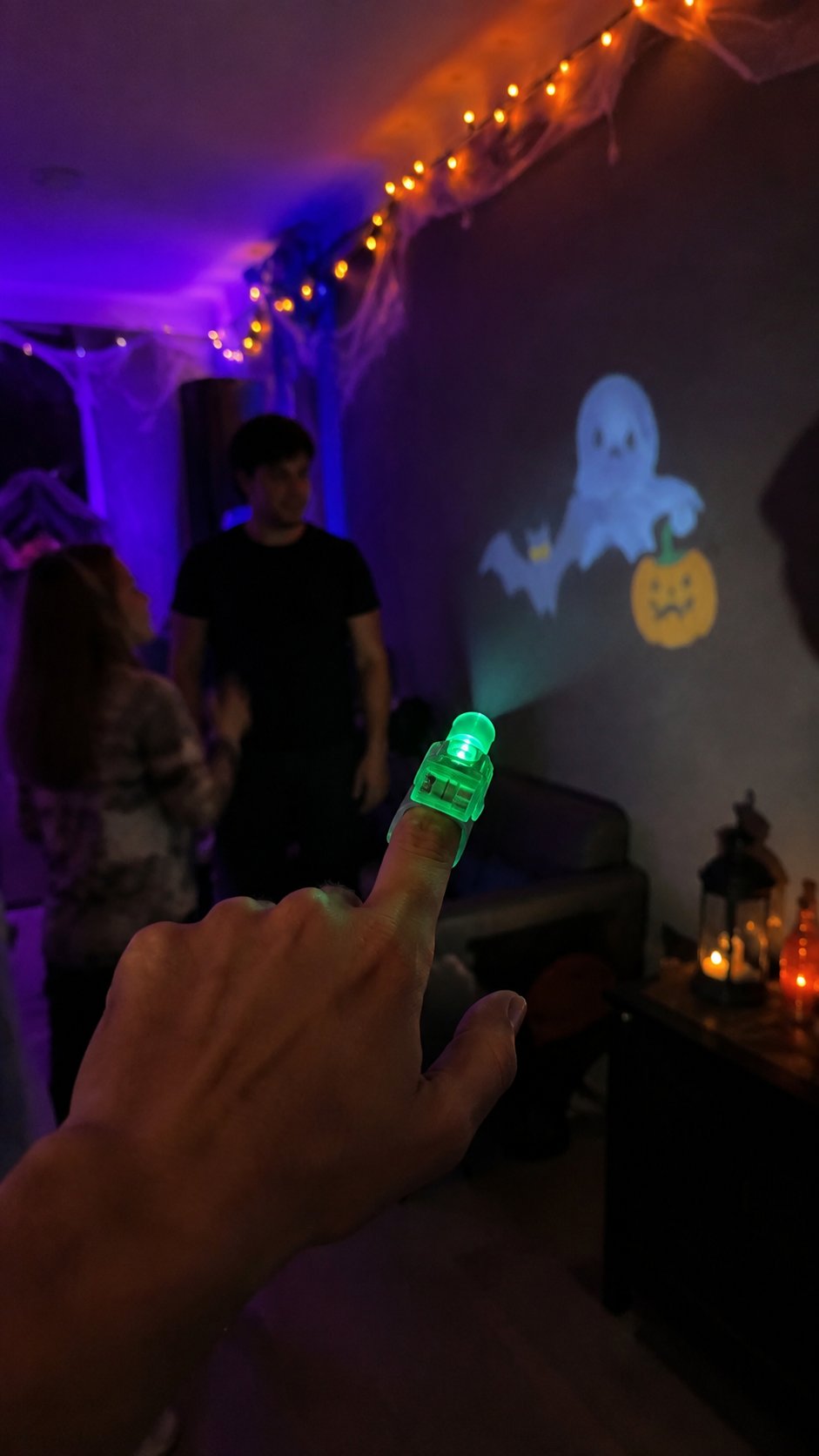 Vertical Halloween party lifestyle photo showing a green finger projector and projected ghost and pumpkin patterns Vertical Halloween party lifestyle photo showing a green finger projector and projected ghost and pumpkin patterns